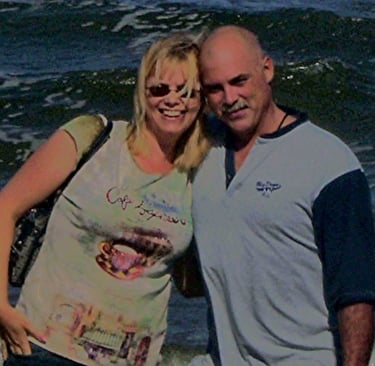 A smiling couple posing together on a beach with ocean waves in the background. Portsmouth, VA