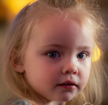A close-up portrait of a young blonde girl with blue eyes and a floral shirt.