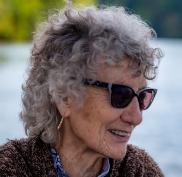 Close-up profile of an elderly woman with curly grey hair wearing stylish sunglasses outdoors. 