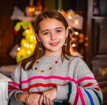 A smiling young girl in a striped sweater posing in front of festive holiday lights.