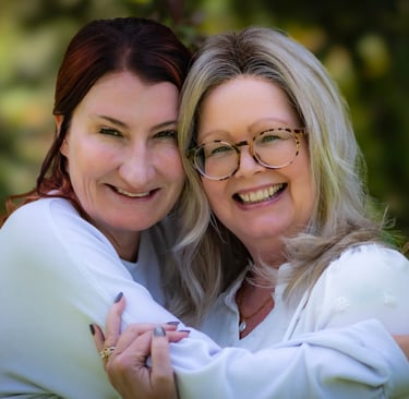 Two happy adult women smiling and hugging outdoors in a garden setting.