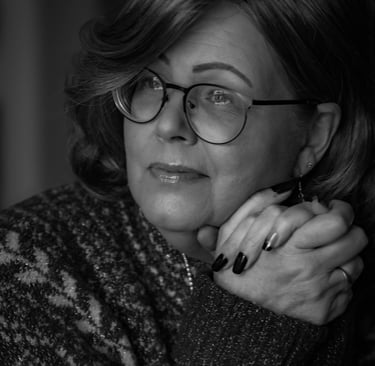 Black and white portrait of a woman with glasses and manicured nails wearing a patterned sweater.