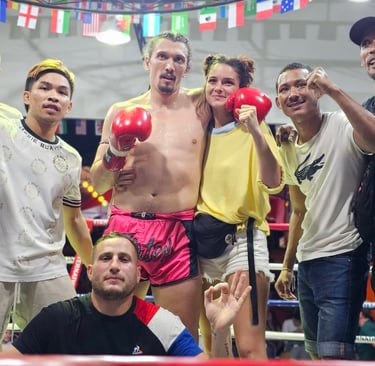 A victorious Muay Thai fighter in red gloves and pink shorts poses with his team in a boxing ring.