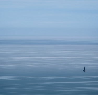 Small, lonely boat with black sails on a vast sea.