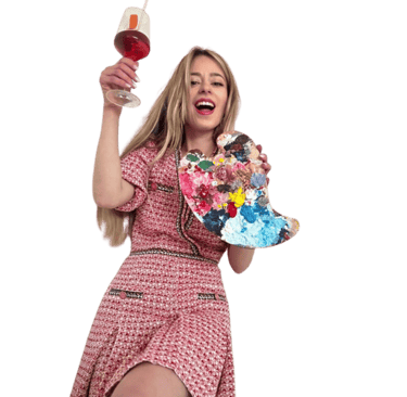 Smiling woman holding a colorful paint palette and raising a glass of wine for a paint and sip event.