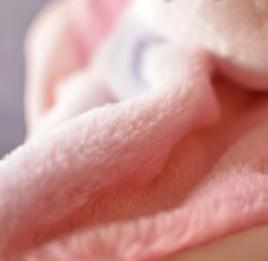 Gros plan sur le tissu d’un doudou artisanal en coton rose pastel, texture douce