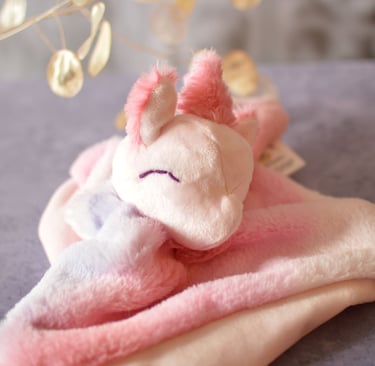 Doudou licorne artisanal en tissu rose pastel, visage brodé, posé dans une ambiance douce.