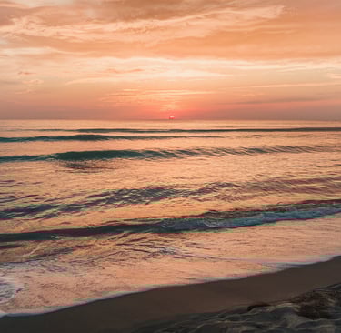 A tranquil beach scene at sunset, with calm waves lapping at the shore and a warm, golden sky
