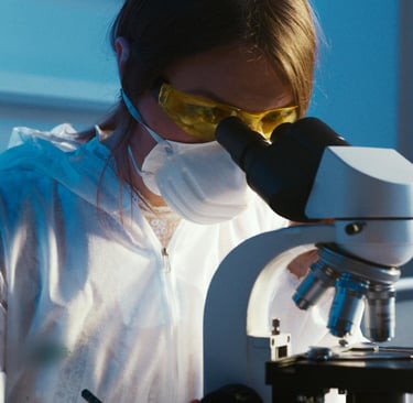a woman in a lab coat and goggles, holding a microscope and looking at