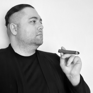 Black and white photo of a 30-year-old Caucasian man with short hair, wearing black, and smoking a cigar