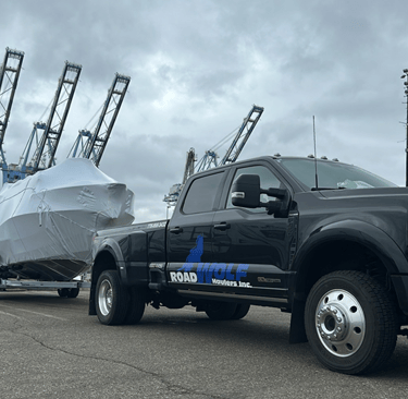 Roadwolf Haulers SuperDuty dually towing a shrink-wrapped boat on a trailer at a shipping port.
