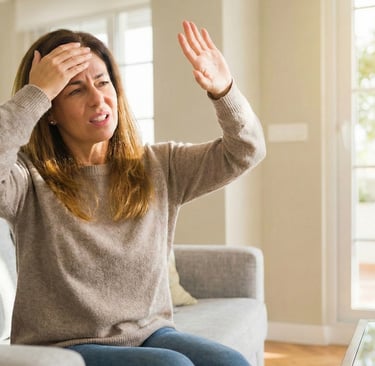 A woman sitting on a sofa wincing and shielding her eyes from bright window light