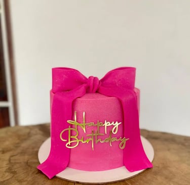 Bolo de aniversário decorado em rosa com fita e detalhes dourados. Ideal para festas e comemorações 