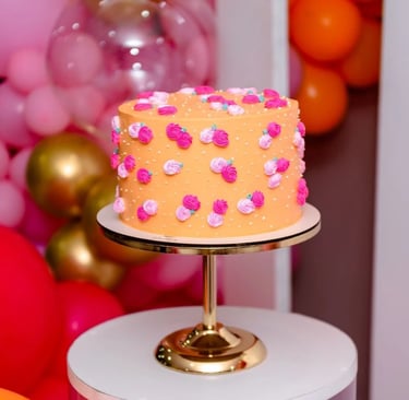 Bolo decorado com rosas coloridas em um suporte dourado, rodeado por balões em tons vibrantes. Ideal
