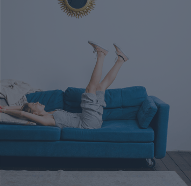 Mujer relajada sobre sofá azul en salón minimalista, transmitiendo confort y bienestar en el hogar — imagen representativa de
