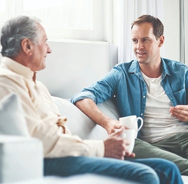 a man and son sitting on a couch talking over coffee