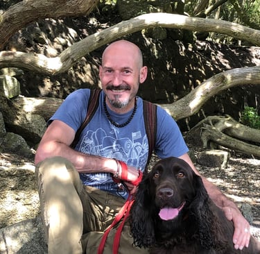 Smiling man with a brown spaniel sitting under a tree