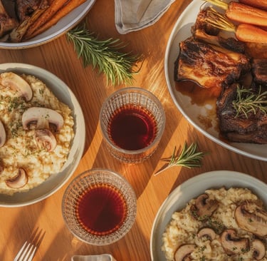 Warm winter dinner flat-lay with braised short ribs, risotto, roasted vegetables, and a steaming gla