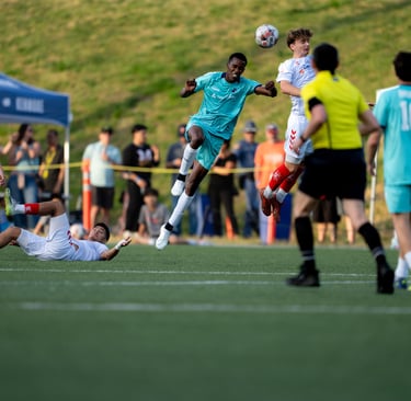 Soccer players in action, one is lying on the ground, two sets of feet leaping.