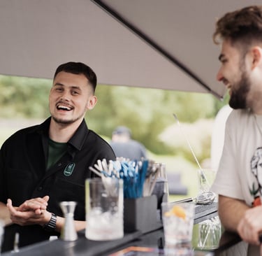 Barmenas mobiliajame bare lauke nuoširdžiai juokiasi ir bendrauja su svečiu.