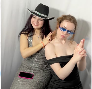 Two women posing for a photo in a silver sequin dress and black dress with a cowboy hat and pixel sunglasses.