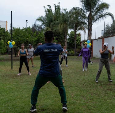 A group of diverse women participating in an outdoor Strive Class fitness session on a grassy lawn.