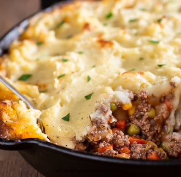 Cauliflower mash being spread over ground beef in a skillet for Thrive Shepherd’s Pie