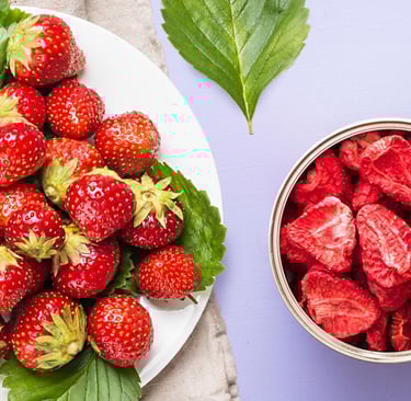 A plate of fresh strawberries and green leaves next to an open container of Thrive freeze-dried food