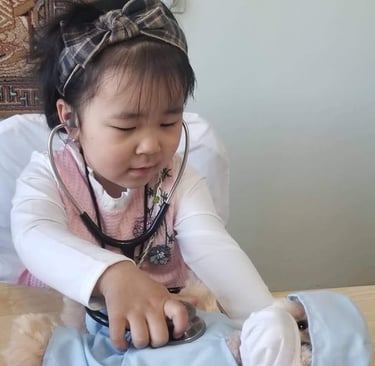 a little girl in a pink dress playing doctor to a teddy bear
