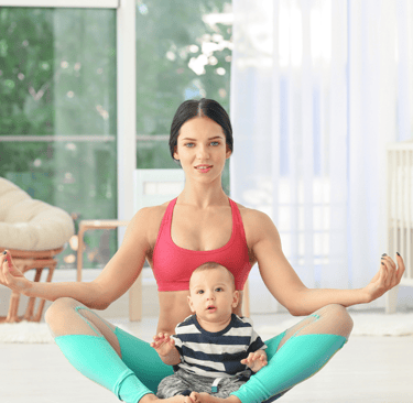 a woman sitting on a yoga mat with her baby
