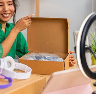 a woman showing a headphone inside a box while looking at her camera with a ring light