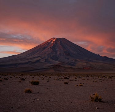 A majestic volcanic mountain peak under a vibrant pink and orange sunset sky in a desert landscape.