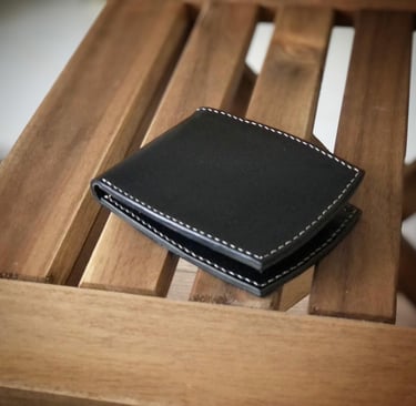 Handmade black leather wallet with white hand-stitched edges, resting on a wooden surface.