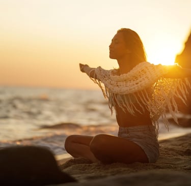 a woman sitting on a beach with her arms outstretched out
