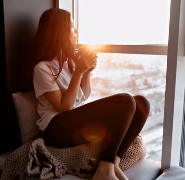 a woman admiring sunrise from room with coffee