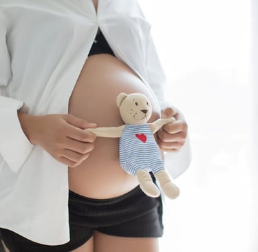 a pregnant woman holding a teddy bear on her belly