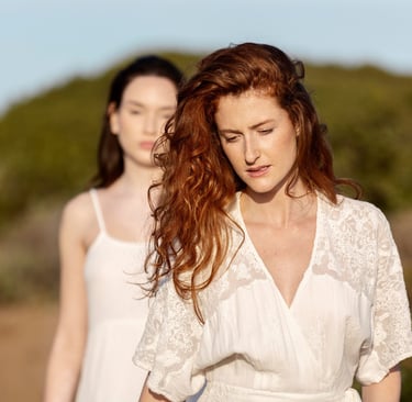 two unhappy women in white dresses standing in a field