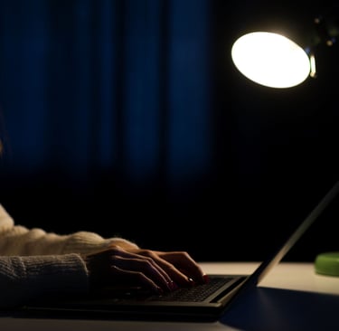 a woman is sitting at night at a desk with a laptop