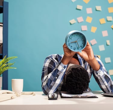 a man sitting at a desk with a clock over his head