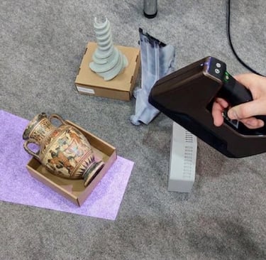A handheld 3D scanner being used to digitize a Greek ceramic amphora vase and various 3D printed objects.