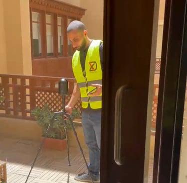 A surveyor in a yellow safety vest uses a 3D laser scanner on a tripod for a building site survey.
