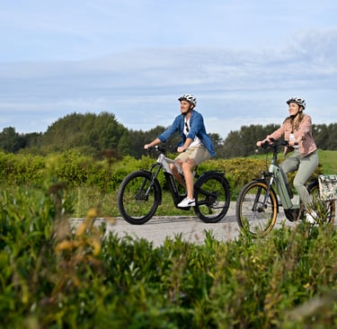 A couple riding electric bikes on a scenic gravel trail through a lush green park.