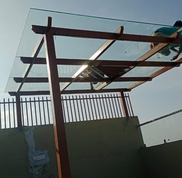 Minimalist glass pergola with a dark metal frame installed on a modern residential terrace.