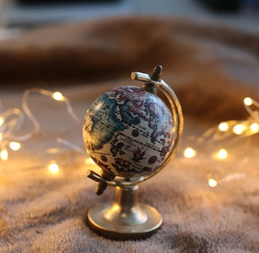 Vintage mini globe on a brass stand surrounded by warm fairy lights on a brown blanket.