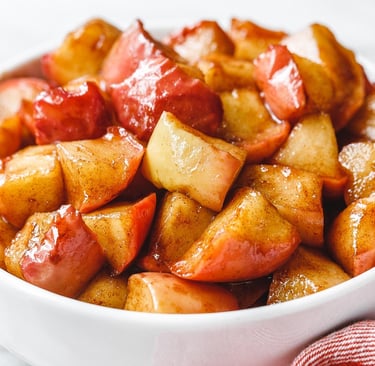 A white bowl filled with warm, glazed cinnamon fried apples, a perfect autumn dessert or side dish.
