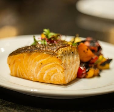 Pan-seared Atlantic salmon fillet served with roasted Mediterranean vegetables on a white plate.