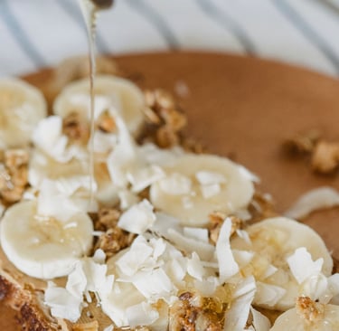 Drizzling honey over healthy sourdough toast topped with sliced bananas, coconut flakes, and granola.