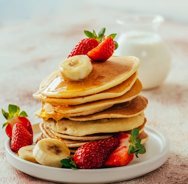 Stack of fluffy buttermilk pancakes topped with maple syrup, fresh strawberries, and banana slices.