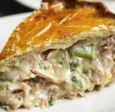 A slice of creamy chicken and leek pie with a golden flaky crust on a white plate.