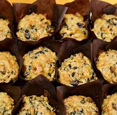 Freshly baked homemade banana nut muffins with dark raisins in brown paper liners.